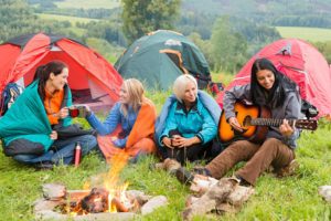 Girls on vacation camping with tents listening girl playing guitar